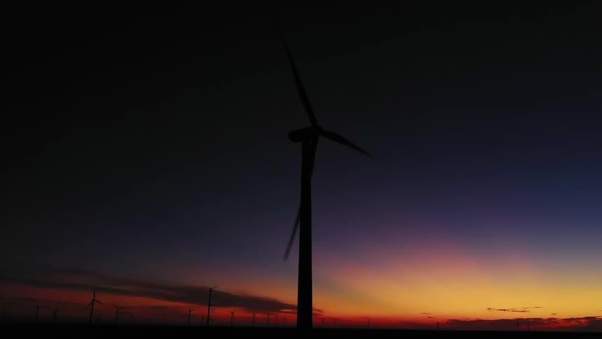 Wind turbines are in a line outside with the sun at the horizon