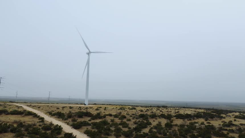 A wind turbine spins in a vast shrubland on a foggy day