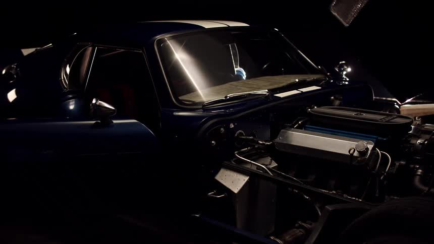 Bright line shines across blue car with racing stripe sitting with open doors and engine