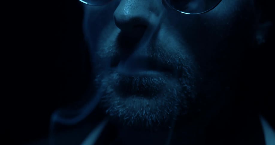 Man smokes a cigarette in dark room directly under a light source