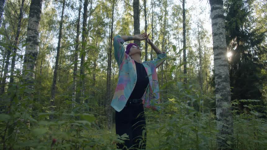 A young woman dances among the vegetation in a woodland during the day
