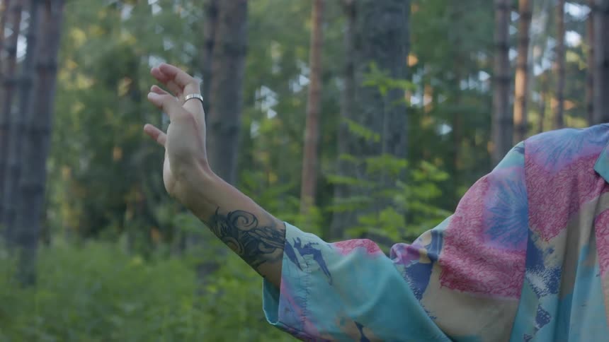 A woman twirls her hand while standing in a woodland during the day