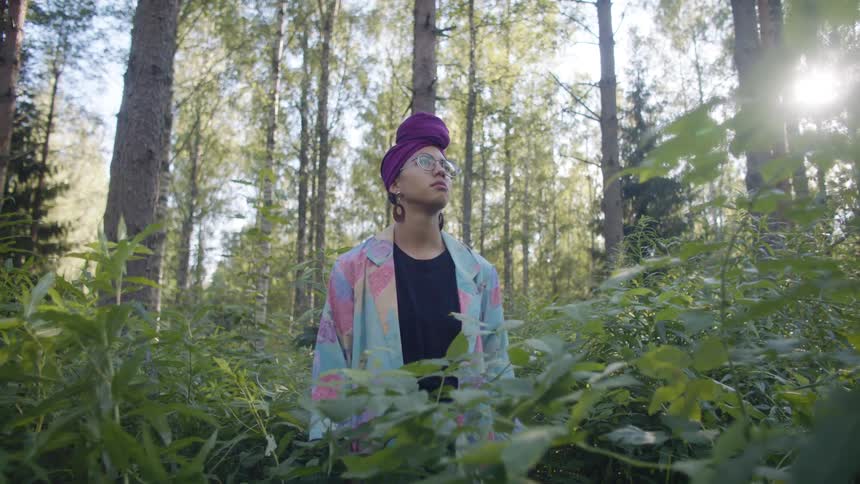 Woman standing in a forest during the day in between tall green plants and staring around