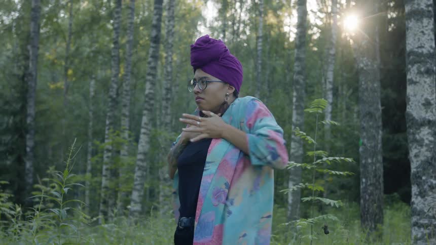 Woman dances in clearing in forest as sun shines through trees