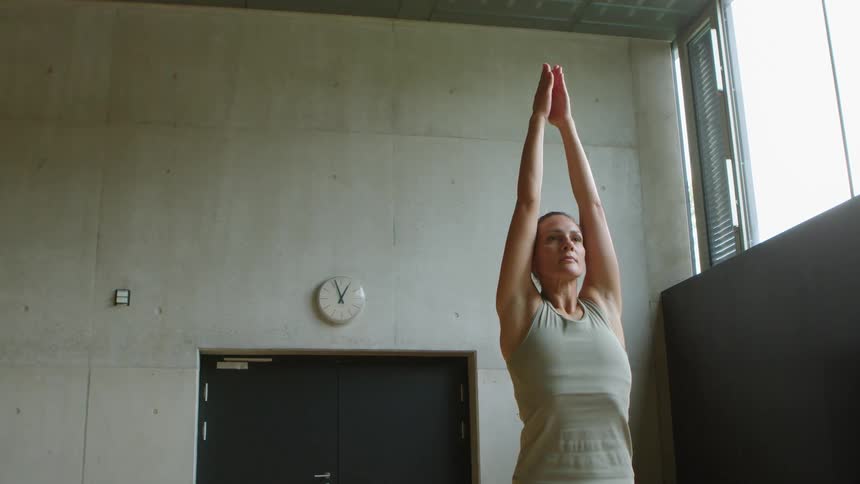 A woman does yoga in a gym during the day