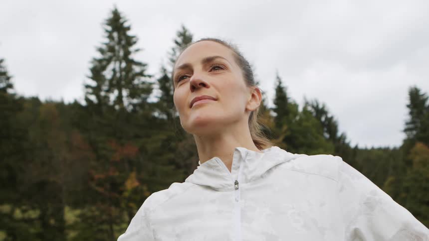 A woman standing and smiling with trees the sky and clouds in the background