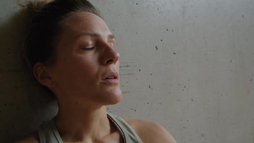 A woman sitting next to a wall blinking