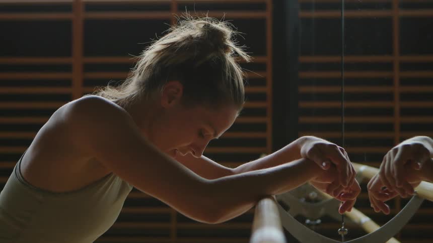 A woman leans against the railing in front of a mirror at a dancing studio