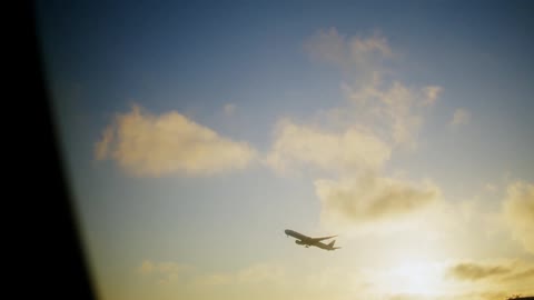 An airplane ascends in the sky with clouds and a low sun