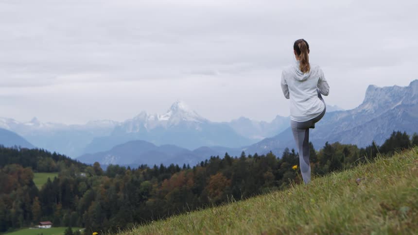 A woman stretches as she looks at the mountains