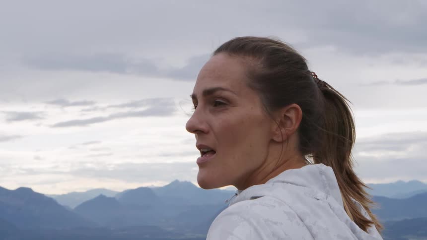 Woman with a ponytail and a white zip up hoodie looks at the mountains after workout