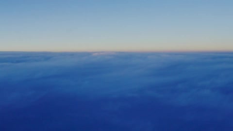 Airplane window view of clouds above a sun setting horizon