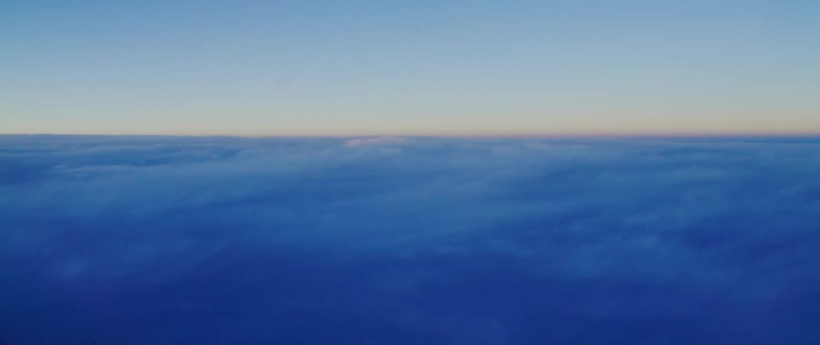 Airplane window view of clouds above a sun setting horizon