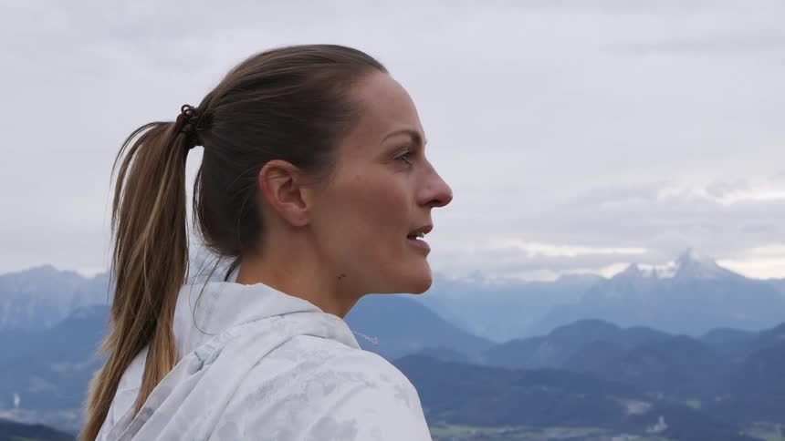 Woman with a ponytail and a white zip up hoodie looks at the mountains after workout