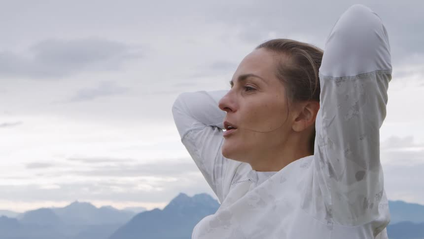 A female caucasian standing outside breathing and stretching near mountains