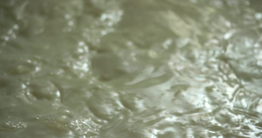 Metal blade rotates through white liquid stirring it causing ripples and bubbles