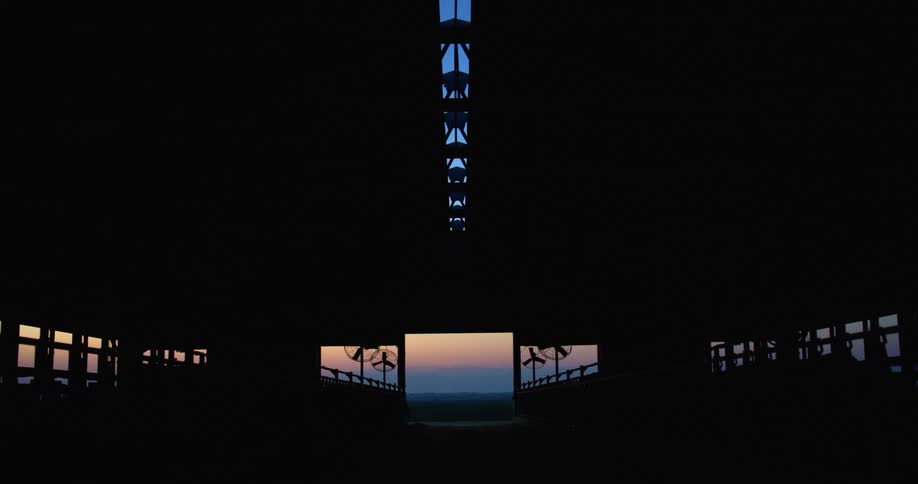 The sunset is visible through the entrance and skylight of an open air pavilion