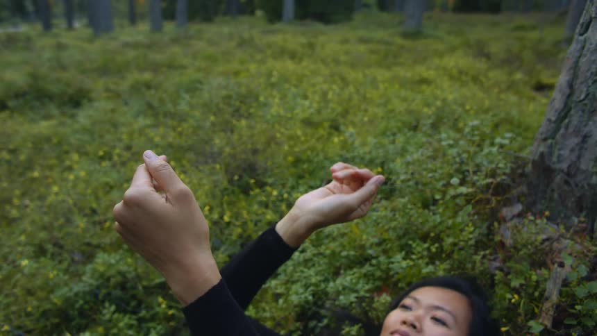 A young asian woman relaxes on her back in the grass and does a slow dance with her hands