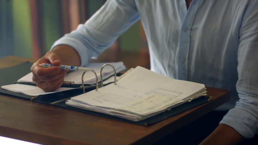 Man sitting at a small table reading through a binder with paperwork