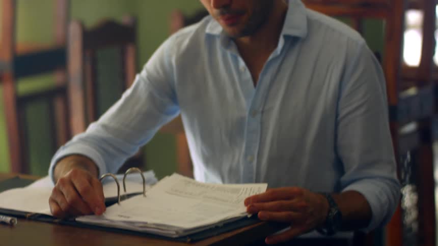 A young man sits in a classroom and reads papers in a binder