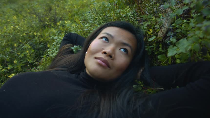 A woman is laying down outdoors in the grass