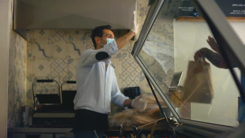 Man wearing face mask behind a counter passing a bag of food to a customer