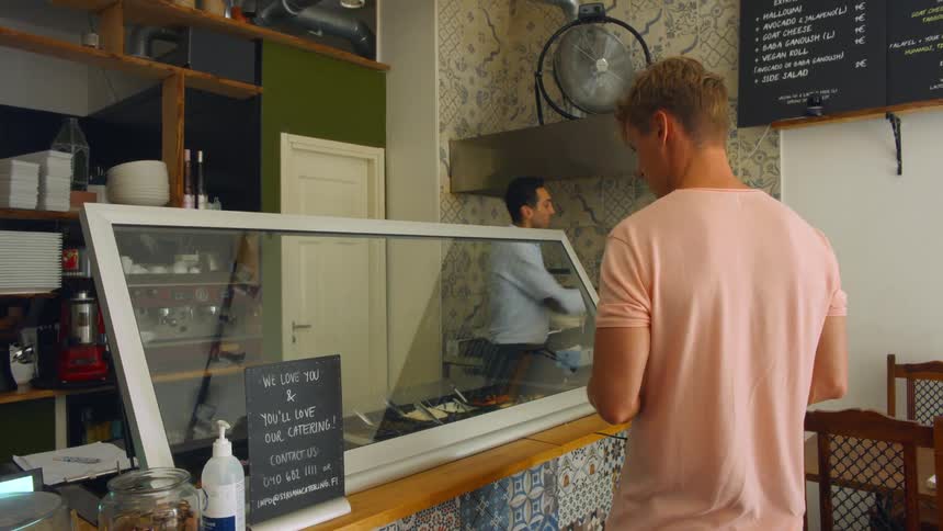 A man standing in a store as another man puts some gloves on and takes a tray to put food in