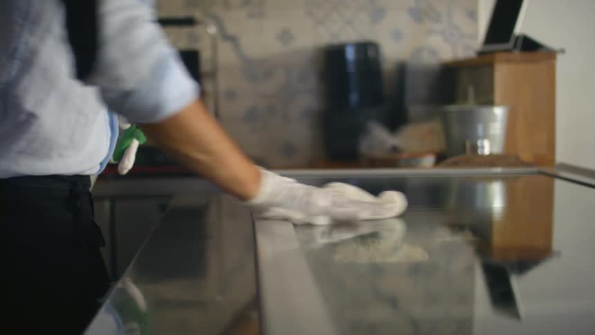 A business owner wears a face mask while wiping down the counter in his restaurant