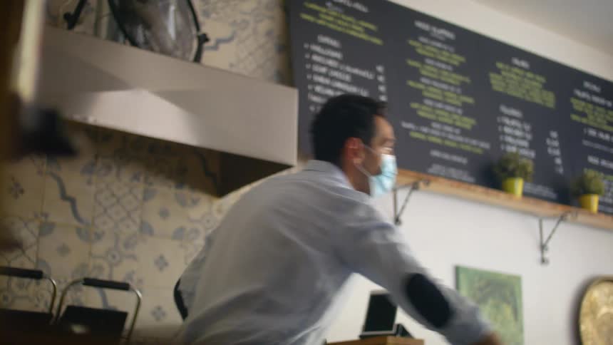 A man wearing a face mask sprays and wipes down surfaces in a restaurant