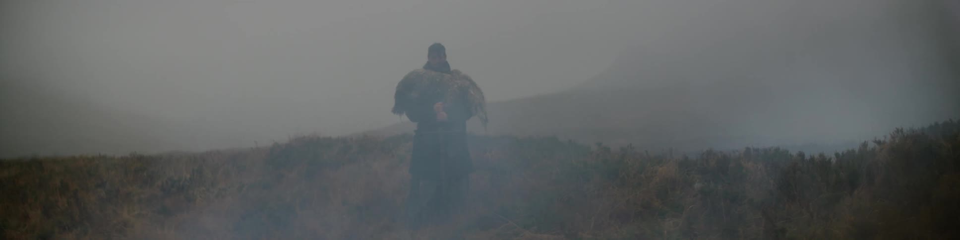 A man holding a sword standing in a foggy field