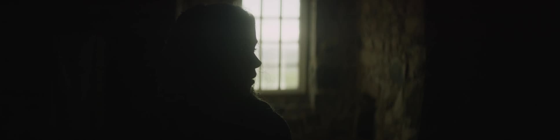 A woman is in a dark room with one window