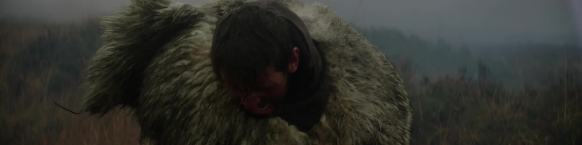 A man wearing a fur wrap swings a stick in a foggy field