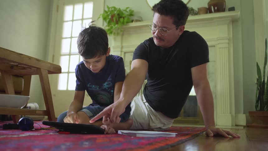 A man and a child sit on the floor while using a tablet together