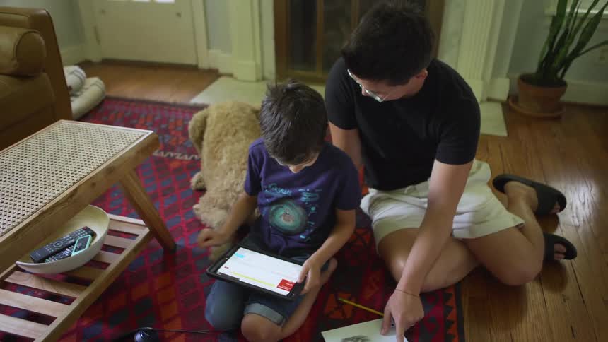 Father and son sitting on red rug use tablet and pet brown dog in the living room at home