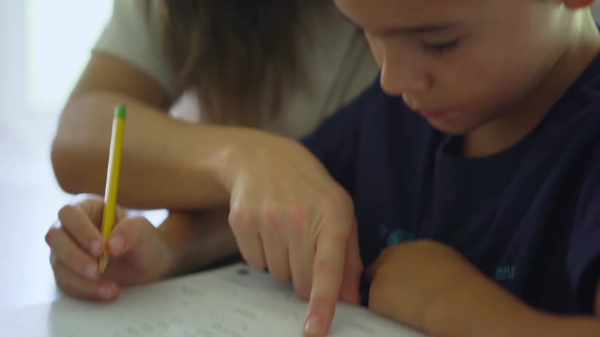 Mother sitting at a table with her son helping him with homework