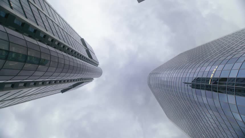 A modern skyscraper with mirrored windows sits near an older high rise apartment building in a city