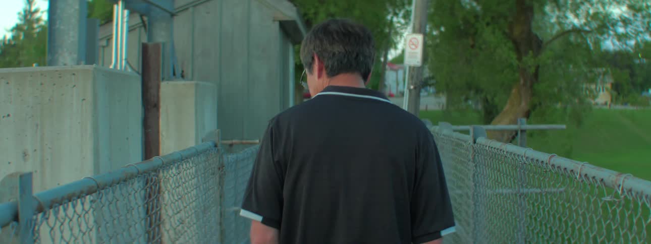 Man walking in a park down a path in between two metal fences