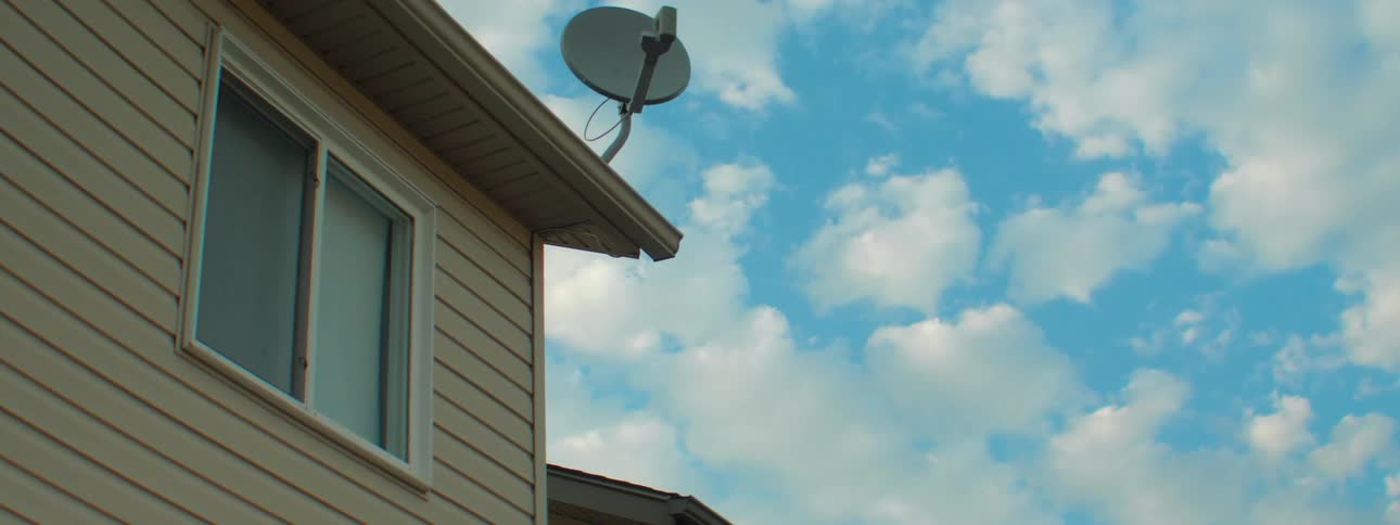 House with window and a satellite dish on the roof on a bright cloudy day