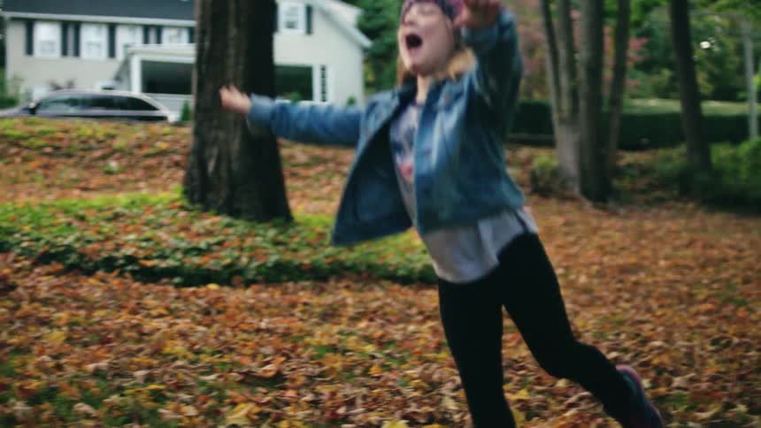 A female child runs through the leaves and jumps onto the ground
