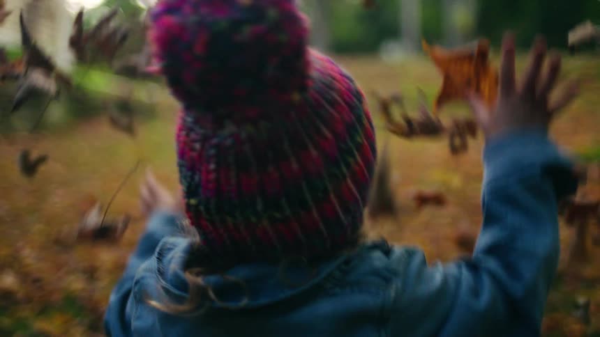Little girl playing outside with autumn leaves next to a house