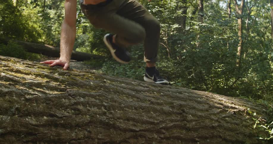 A man running through a forest jumps over a fallen tree