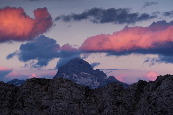 Clouds moving above a mountain peek while the sun sets