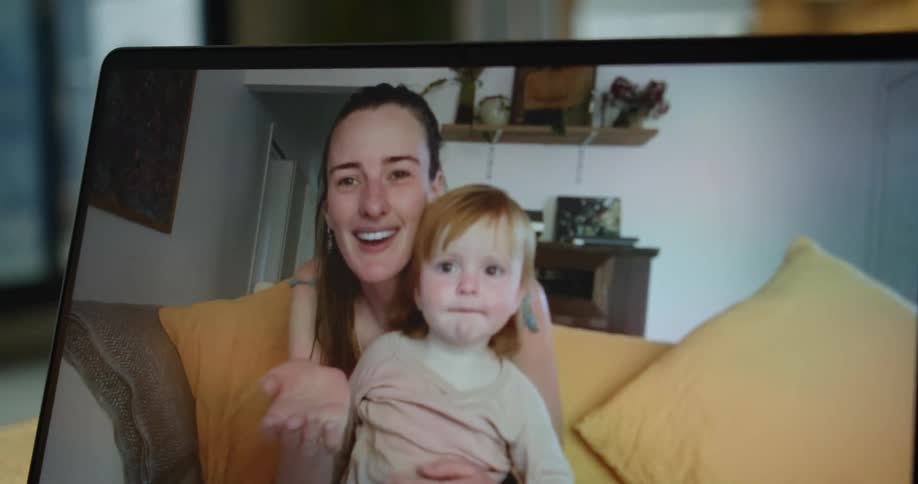A mother and child are on a computer screen waving while sitting in a living room
