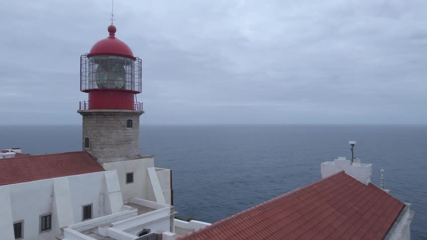 Shot over a building with red roof and light house overlooking an ocean with overcast skies