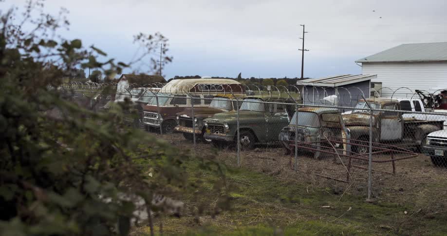 Old rusted vehicles parked inside of a yard with a gated fence