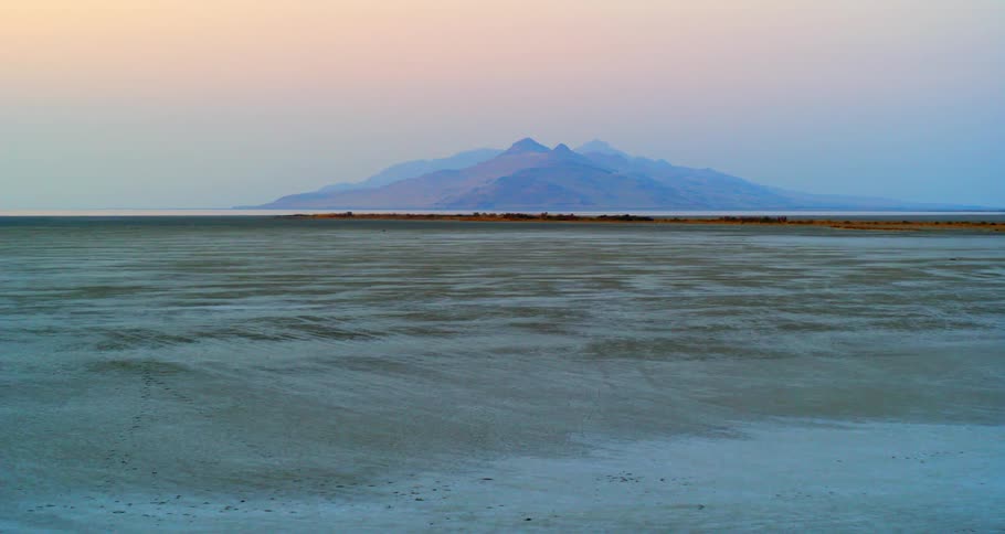 Wide open empty field of beige ground at daytime with mountains in the distance