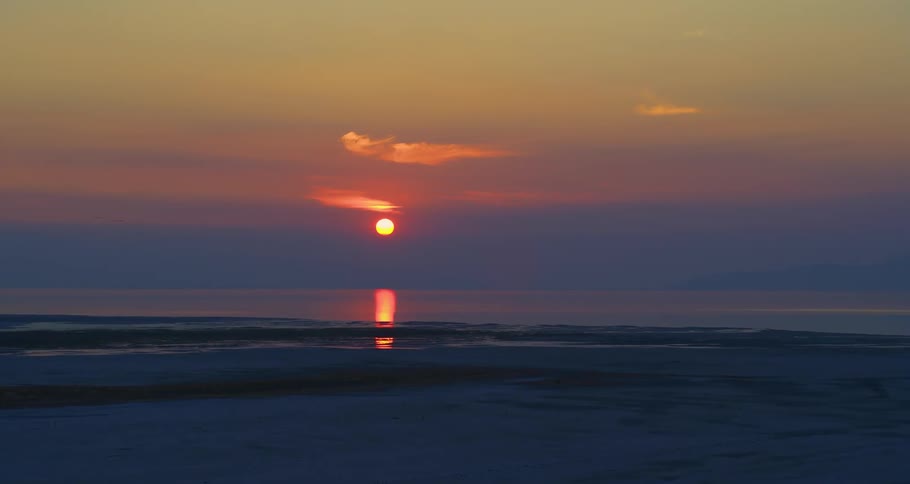 Sun setting in the distance above an ocean next to a shoreline