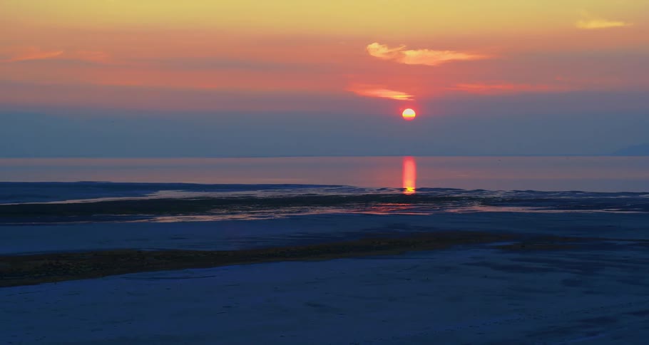 The setting sun glows bright orange as it shimmers on the ocean surface