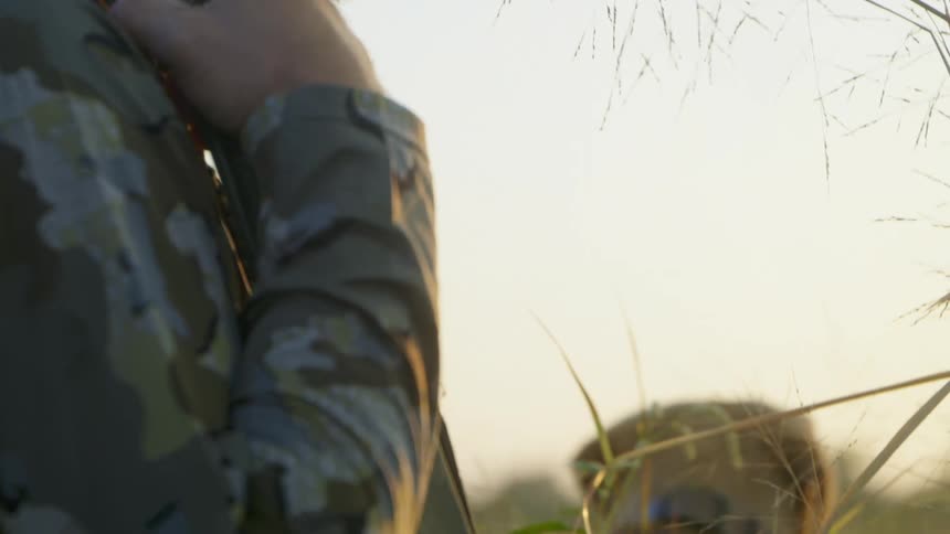 A man hunting with a gun stands outside wearing camouflage clothes with his dog