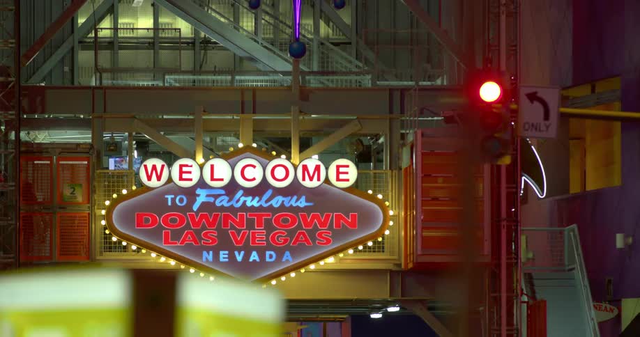 A welcome sign to las vegas at night with flashing lights next to traffic signal and sign